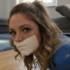 Young woman with wavy light brown hair and green eyes gagged with beige microfoam tape over her mouth