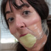 Dark-haired woman with two large fluorescent socks massively stuffed in her mouth and clear tape wrapped tightly around her head