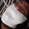 Dark-haired woman looking upward with her mouth and lower face covered by multiple layers of thick white microfoam tape