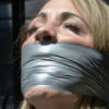 Blonde woman with eyes closed tightly gagged under multiple layers of shiny silver duct tape covering her mouth and chin