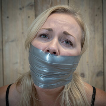 Blonde woman with multiple layers of silver duct tape wrapped tightly over her mouth, looking upward