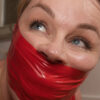 Blue-eyed woman gagged with shiny red tape covering her mouth and lower face, eyes looking upward