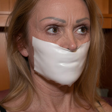 Mature blonde woman gagged with shiny white microfoam tape stretched across her mouth, eyes looking sideways