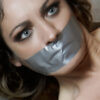 Blue-eyed woman with dark eye makeup tightly gagged with silver duct tape stretched across her lips