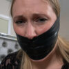 Blonde woman with sweaty face gagged under multiple layers of shiny black tape covering her mouth