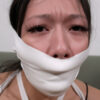 Asian woman with teary eyes gagged under tight white microfoam tape wrapped around her mouth